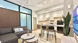A modern living room with a sofa, coffee table, and chairs, a kitchen area with a dining table, and a large window. - Silverscape Residence Sea View Melaka by Stayrene (Melaka)