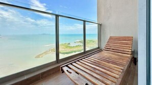 A balcony with a wooden bench and a large window offering a view of the sea and a distant shoreline. - Silverscape Residence Sea View Melaka by Stayrene (Melaka)