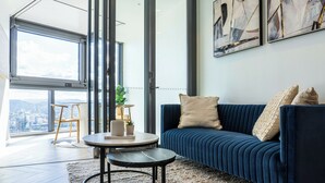 A modern living room with a blue sofa, a round coffee table, and a city view through large windows.