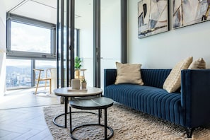 A modern living room with a blue sofa, a round coffee table, and a city view through large windows.