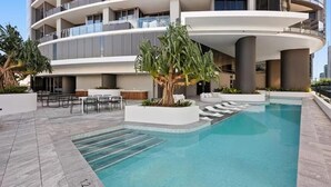 A modern hotel with a swimming pool, outdoor seating, and a palm tree.