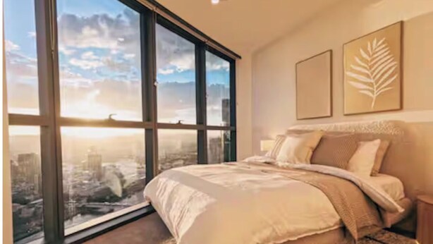 A bedroom with a large window, a bed, and two wall-mounted artworks.