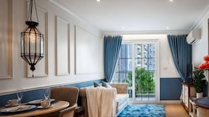 A room with a dining table, chairs, a sofa, a blue rug, and a view through a glass door.