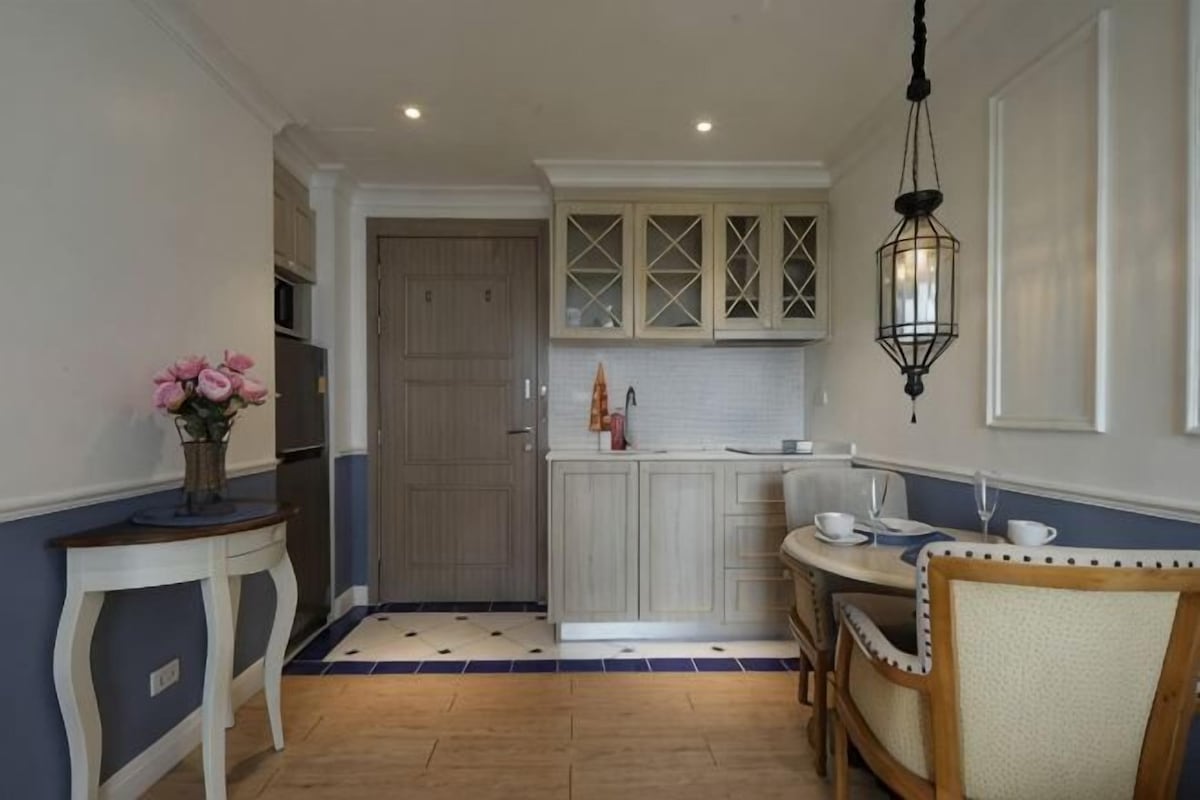 A compact kitchen with white cabinets, a dining table, and a hanging light fixture.
