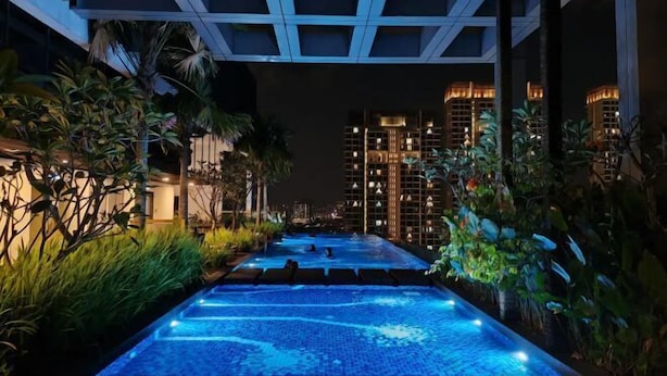 A nighttime swimming pool with blue lighting, surrounded by lush greenery and modern buildings in the background. - Pavillion Bukit Jalil 【Walk 5 mins】Stylish Studio 2-4 Pax (Kuala Lumpur)