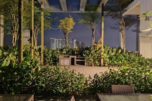 Un espace extérieur aménagé avec des sièges, entouré de verdure et offrant une vue sur les immeubles de grande hauteur.