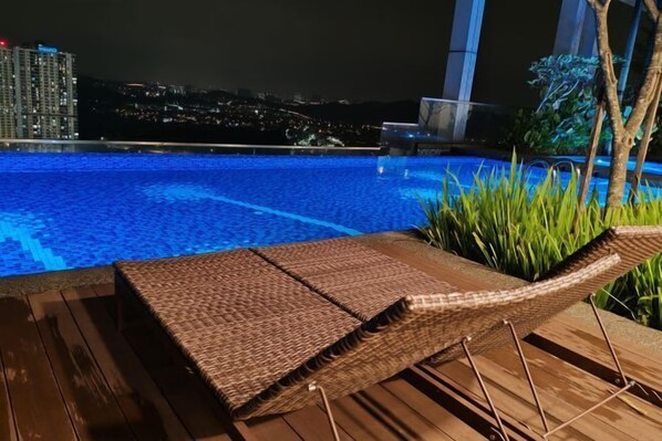 Zona junto a la piscina con una tumbona y vista panorámica de la ciudad de noche.