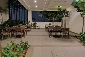 Zona pranzo interna con tavoli e sedie, circondata da piante in vaso.