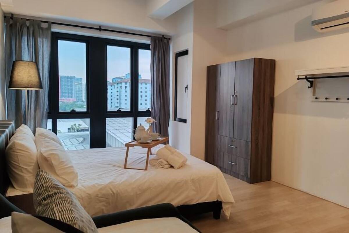 A bedroom with a bed, a bedside table with a lamp, a wardrobe, and a window with a view of buildings.