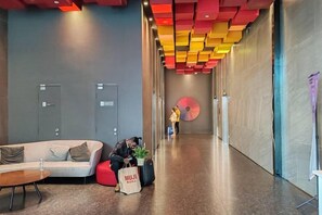 Un hall d’hôtel avec un canapé, un fauteuil en forme de sac de haricots rouge, une bouteille d’eau et une personne assise.