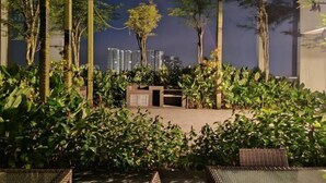 An outdoor seating area with lush greenery and a view of high-rise buildings in the background. - Pavillion Bukit Jalil 【Walk 5 mins】Stylish Studio 2-4 Pax (Kuala Lumpur)