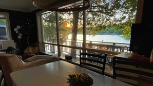 Un coin repas avec une table et des chaises, une plante en pot et une vue sur un lac, visible à travers de grandes fenêtres.
