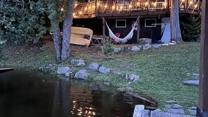 Une cabane en bois avec une terrasse, un hamac et un étang.