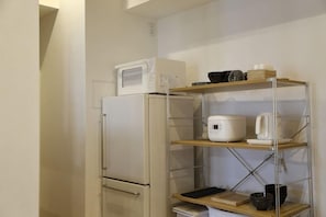 A compact kitchenette with a refrigerator, microwave, and shelves holding kitchenware. - ISSHUKU · Asakusa (Tokyo)