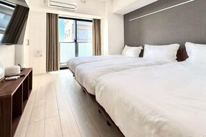 Une chambre d’hôtel avec deux lits, une télévision, un bureau et une porte-fenêtre coulissante donnant sur l’extérieur.
