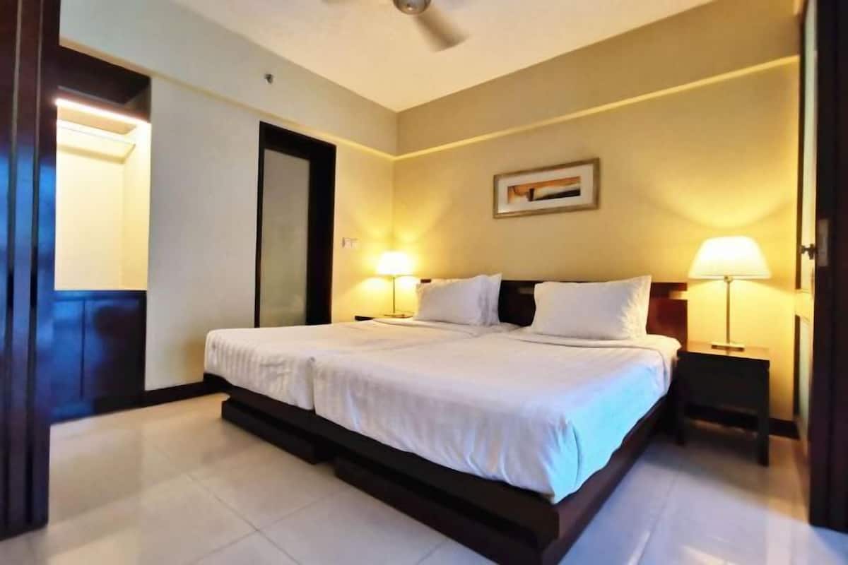 Een hotelkamer met een groot bed, twee bedlampen, een plafondventilator en een ingelijst kunstwerk aan de muur.