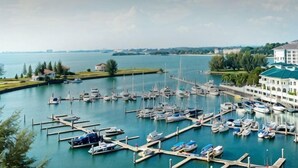 A marina with boats docked at piers, a large building with a green roof, and a body of water in the background. - PD Admiral Cove Private Unit - Up to 4 Pax (Port Dickson)
