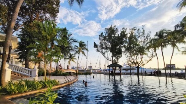A swimming pool with palm trees and a gazebo, surrounded by a white fence and greenery. - PD Admiral Cove Private Unit - Up to 4 Pax (Port Dickson)