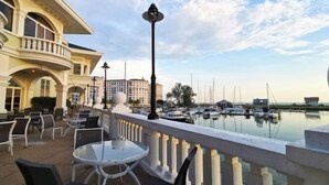 A waterfront balcony with outdoor seating, a lamp post, and a view of boats and buildings. - PD Admiral Cove Private Unit - Up to 4 Pax (Port Dickson)
