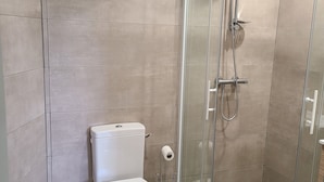 A modern bathroom with a toilet, a glass shower enclosure, and a mop on the floor.