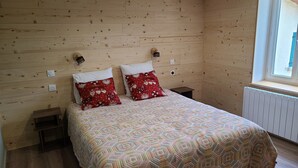A bedroom with wooden panel walls, a bed with patterned bedding, two red pillows, bedside lamps, and a window with a view.