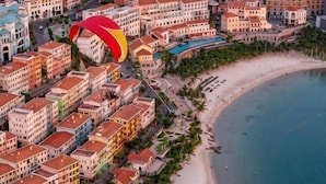A coastal hotel area with buildings, a beach, and a parasail.