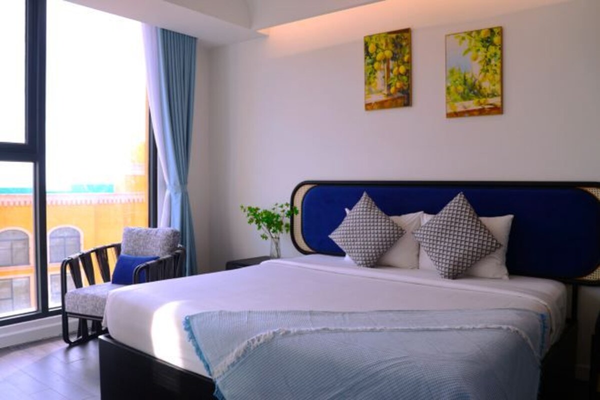 Una camera d'albergo con un letto grande, una sedia, una pianta e opere d'arte alle pareti.