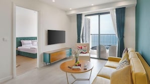 A modern living room with a sofa, a coffee table with books and a vase, a TV mounted on the wall, and a balcony with curtains.