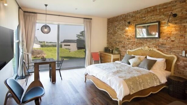 A bedroom with a large bed, a dining table, chairs, a TV, and a view of the outdoors. - Kairosjeju Boutique Stay (Jeju)