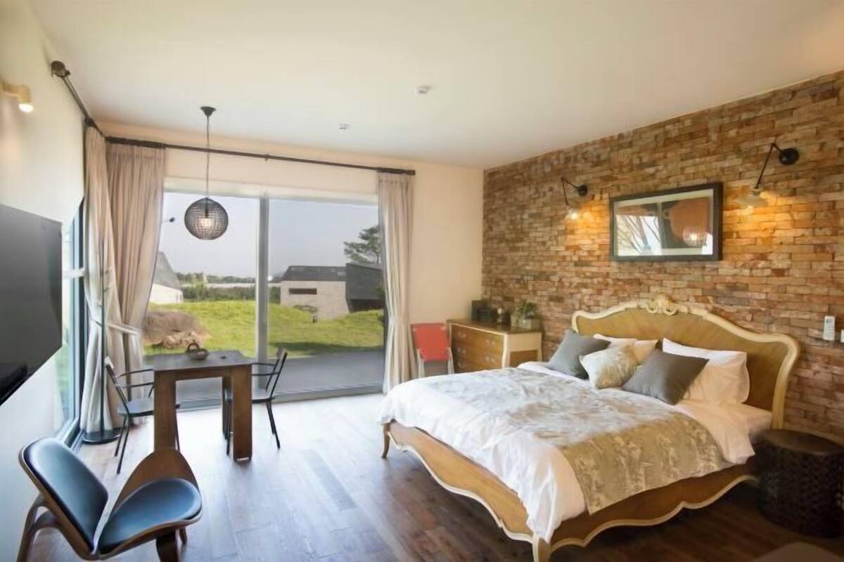 Ein Schlafzimmer mit einem großen Bett, einem Esstisch, Stühlen, einem Fernseher und Blick ins Freie.