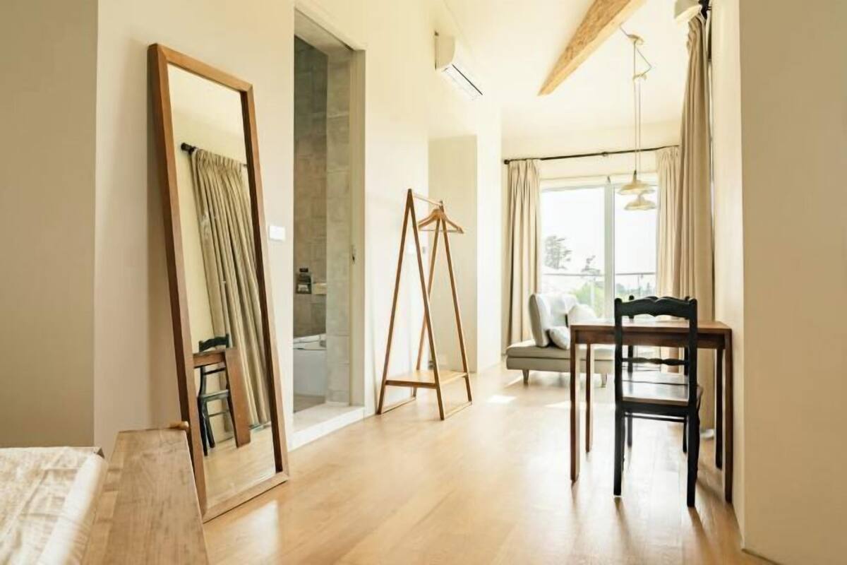 Ein Zimmer mit einem Bett, einem Spiegel, einem Holztisch, einem Stuhl und Blick ins Freie.