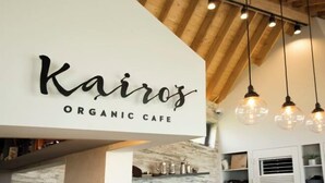 A sign for 'Kairos Organic Cafe' with a modern interior featuring exposed wooden beams and pendant lighting. - Kairosjeju Boutique Stay (Jeju)
