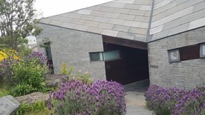 A modern building with a stone facade, a dark entrance, and a pathway leading to the entrance. - Kairosjeju Boutique Stay (Jeju)
