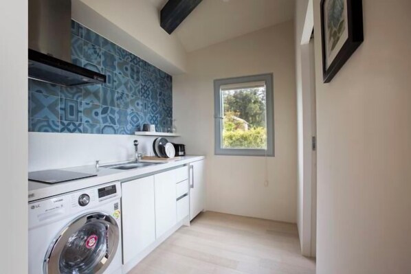 A compact kitchen with a washing machine, a window with a view, and a patterned backsplash.