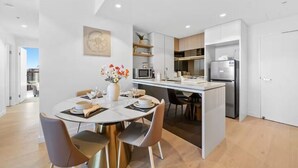 Une cuisine moderne avec des meubles blancs, un îlot central et un coin repas comprenant une table ronde et des chaises.