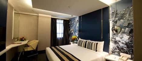 A hotel room with a bed, a desk, a chair, a mirror, a window with curtains, and a cityscape wall.