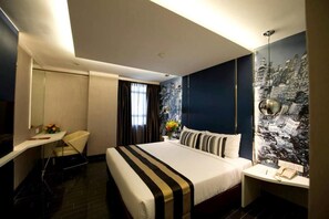 Une chambre d’hôtel comprenant un lit, un bureau, une chaise, un miroir, une fenêtre avec des rideaux et un mur décoré d’un motif représentant un paysage urbain.