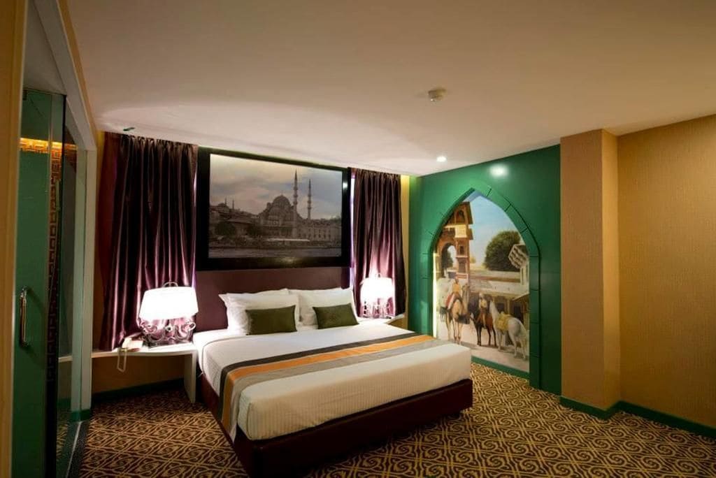 A hotel room with a large bed, two bedside tables, a view of a cityscape, and a mural of a market scene.