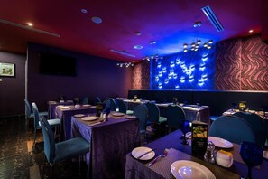 Un restaurant avec des tables dressées, des chaises et un mur décoratif éclairé de lumière bleue.