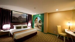 Hotelkamer met een bed, een bureau, een stoel, een nachtkastje, een lamp, een raam met gordijnen en een wanddecoratie.