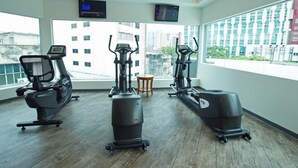 A gym with cardio machines, a TV, and a view of buildings. - Kingston Hotel 3 @ Kuala Lumpur (Kuala Lumpur)