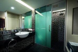 Une salle de bain moderne avec un lavabo blanc, une douche en verre et un mur recouvert de carreaux.
