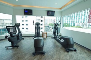 Un gimnasio con máquinas de cardio, un televisor y vistas a edificios.