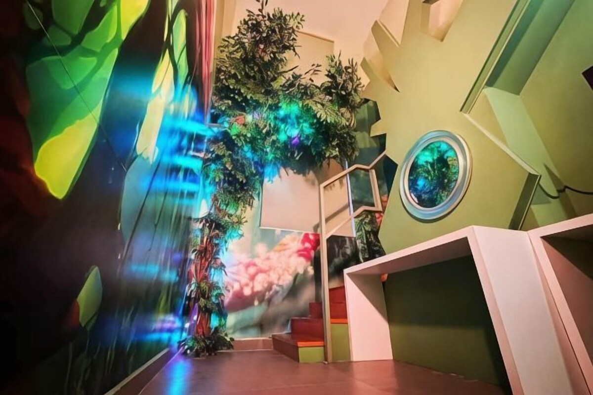Un couloir avec un escalier, une plante en pot et un objet circulaire fixé au mur.