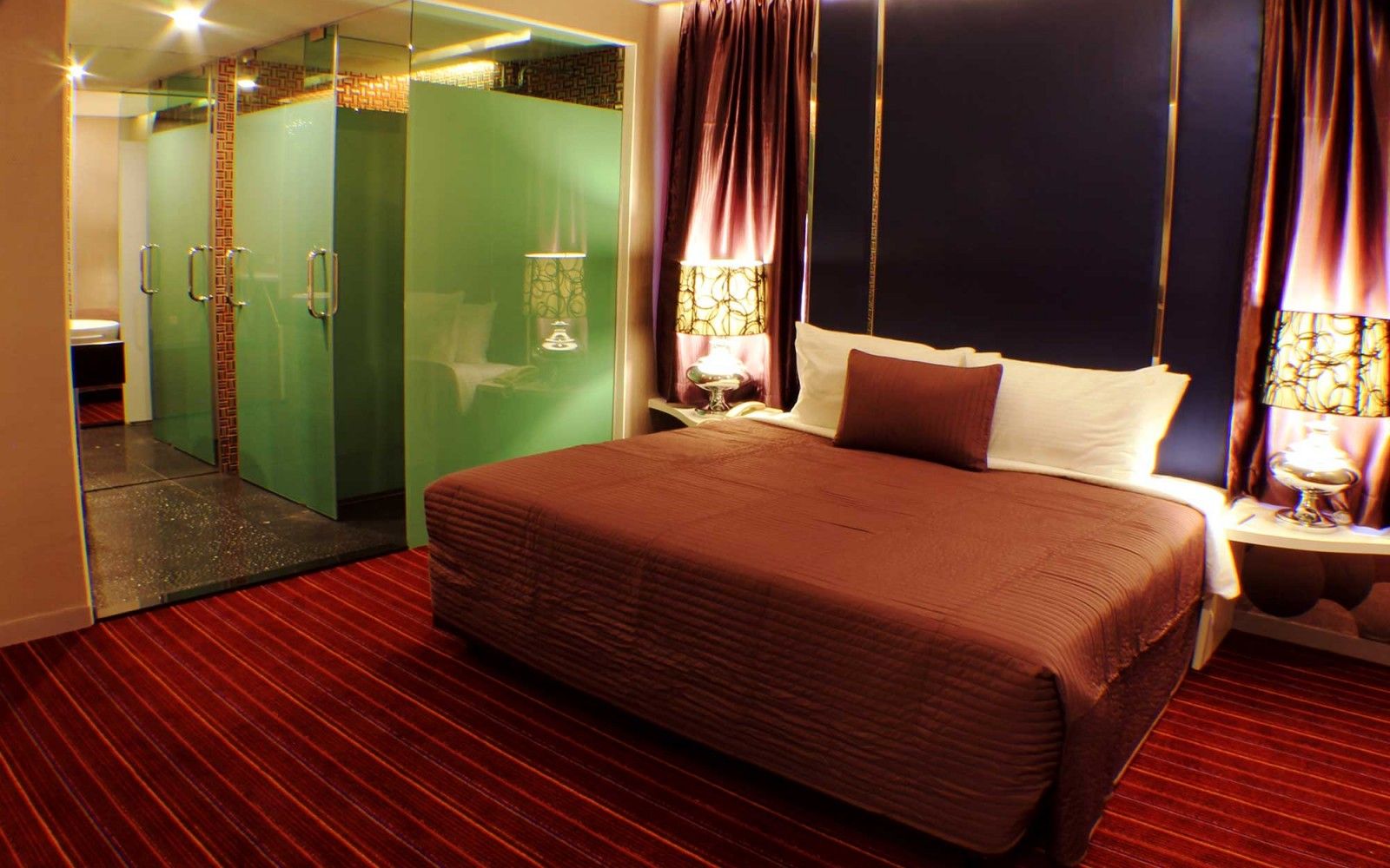 A hotel room with a large bed, a glass-enclosed shower, and a red-striped carpet.