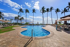 Ein Pool mit gewölbter Kante, umgeben von Liegestühlen und Palmen.