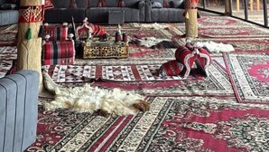 Une pièce avec un plafond haut, de grandes colonnes en bois, un ensemble de canapés et un tapis à motifs.
