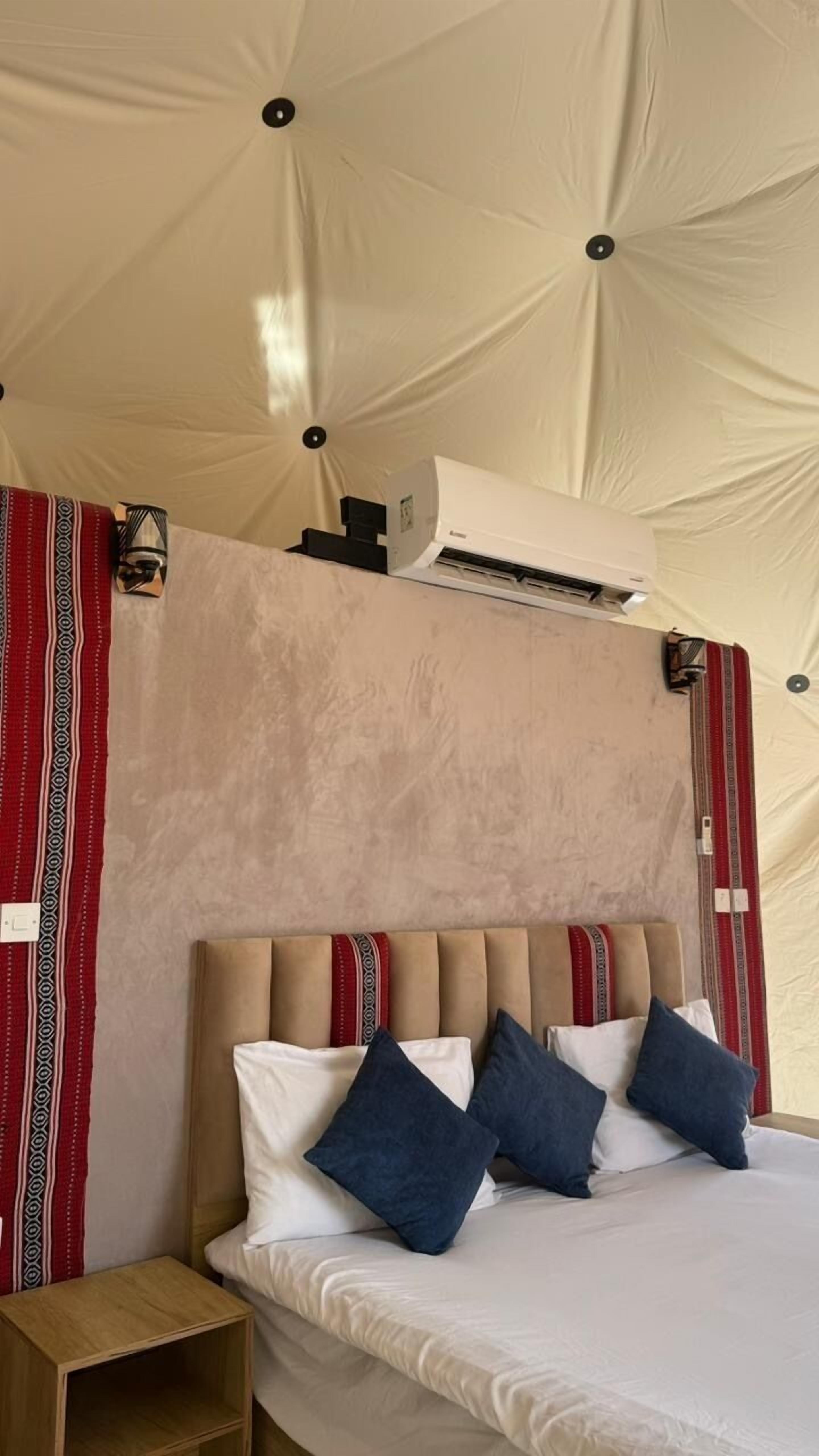 A bed with a headboard, pillows, and a nightstand in a tent-like room.