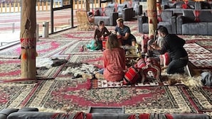 Un intérieur spacieux avec de hauts plafonds et de grandes fenêtres, comprenant un espace central agrémenté d’un tapis à motifs et de différents coins salon.