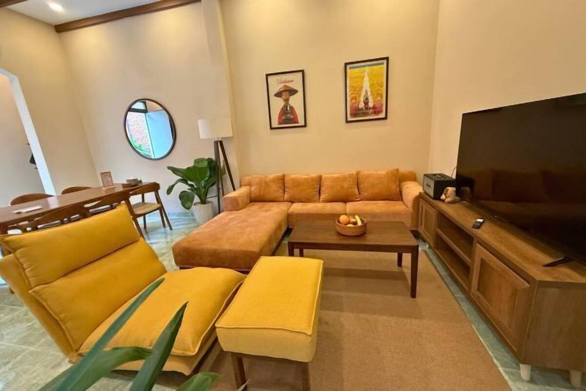 Ein Wohnzimmer mit Sofa, Hocker, Couchtisch, Fernseher und gerahmten Bildern an der Wand.